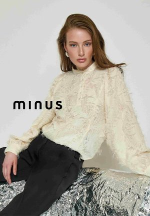 Cream textured blouse with a high collar and button details, paired with black trousers, displayed against a light background.