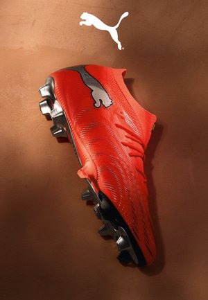 Roter synthetischer Fussballschuh mit strukturierter Oberseite, schwarzen Akzenten und metallischen Stollen. Mit einem auffälligen Puma-Logo an der Seite.