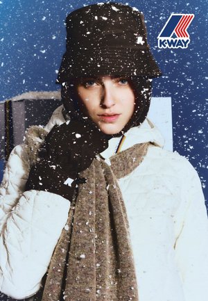 Veste matelassée blanche, écharpe tricotée marron, gants marron et chapeau seau foncé. Des flocons de neige tombent sur un fond bleu. Logo K-Way dans un coin.