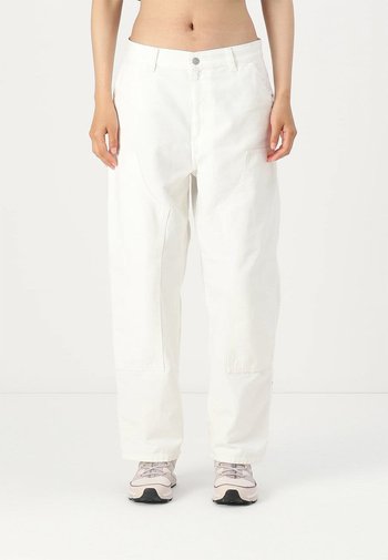 Witte, losse denimbroek met voorzakken en een enkele knoopsluiting, gedragen met lichtgekleurde sneakers.