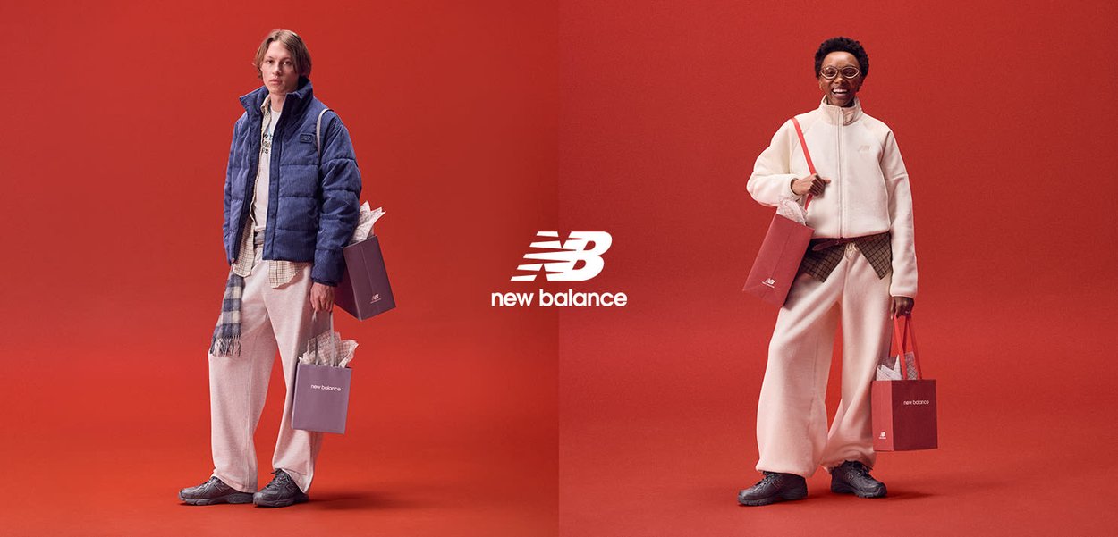 Due modelli sono in piedi di fronte a uno sfondo rosso. Uno indossa una giacca imbottita blu e pantaloni larghi color crema, mentre l'altro sfoggia una felpa bianca con cerniera e pantaloni color crema.