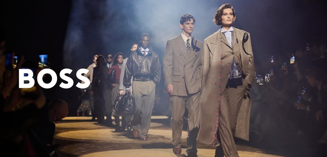 Des mannequins défilent sur le podium vêtus de costumes et de manteaux élégants et sur mesure lors du défilé de mode BOSS, dans une ambiance tamisée et enfumée.