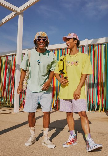 Deux personnes portant des tenues décontractées. L'une en chemise vert menthe et en shorts bleus à motifs, l'autre en chemise jaune et en shorts lavande.