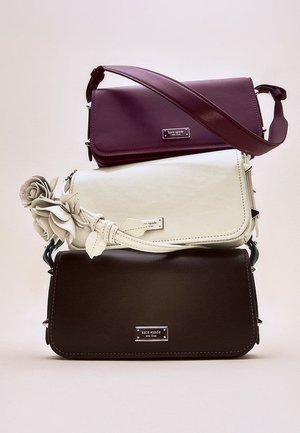 Drei übereinander gestapelte Handtaschen: eine bordeauxrote Ledertasche mit langem Riemen, eine weiße Tasche mit floralem Akzent und eine dunkelbraune Tasche, alle mit Logofähnchen versehen.