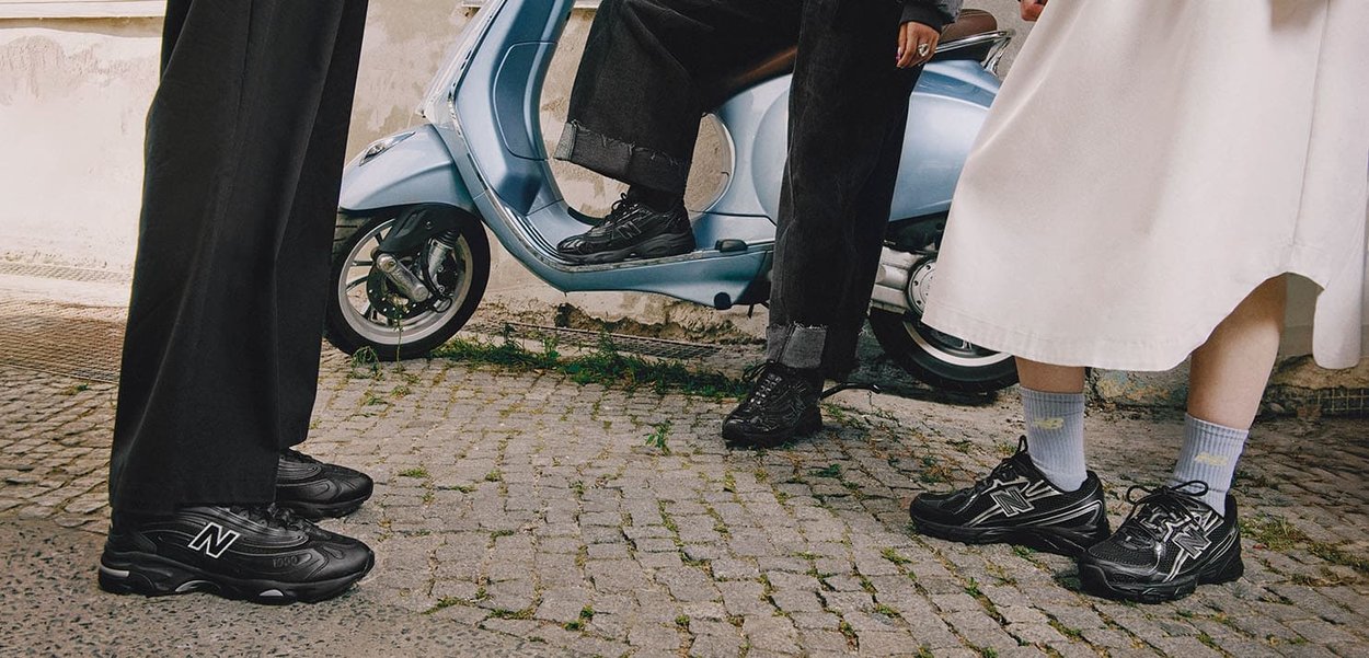 Black athletic shoes with textured uppers and distinct logo, worn by multiple individuals in a street setting near a blue scooter.