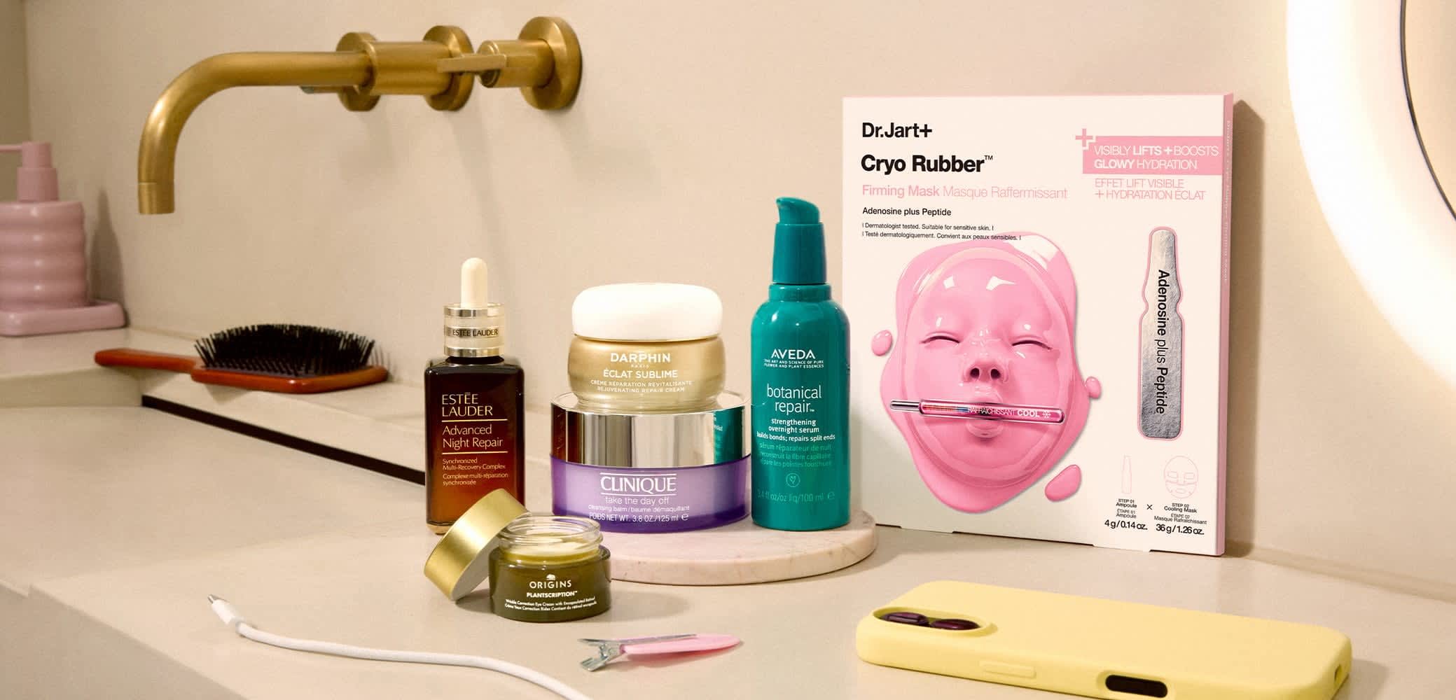 Diverse huidverzorgingsproducten, waaronder Estée Lauder serum, Darphin crème, Clinique balsem, Aveda serum, Origins oogcrème, Dr.Jart+ Cryo Rubber-masker en een geel telefoonhoesje.
