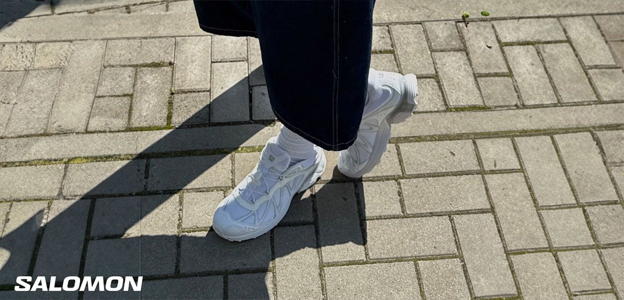 White Salomon sneakers with a textured surface and minimal design, featuring a lace-up closure and cushioned sole, paired with white socks.