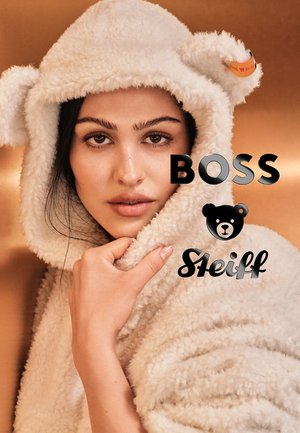 Weißer, flauschiger Kapuzenüberwurf mit Bärenohren, der eine weiche Textur aufweist. Die Logos von BOSS und Steiff sind gut sichtbar platziert.