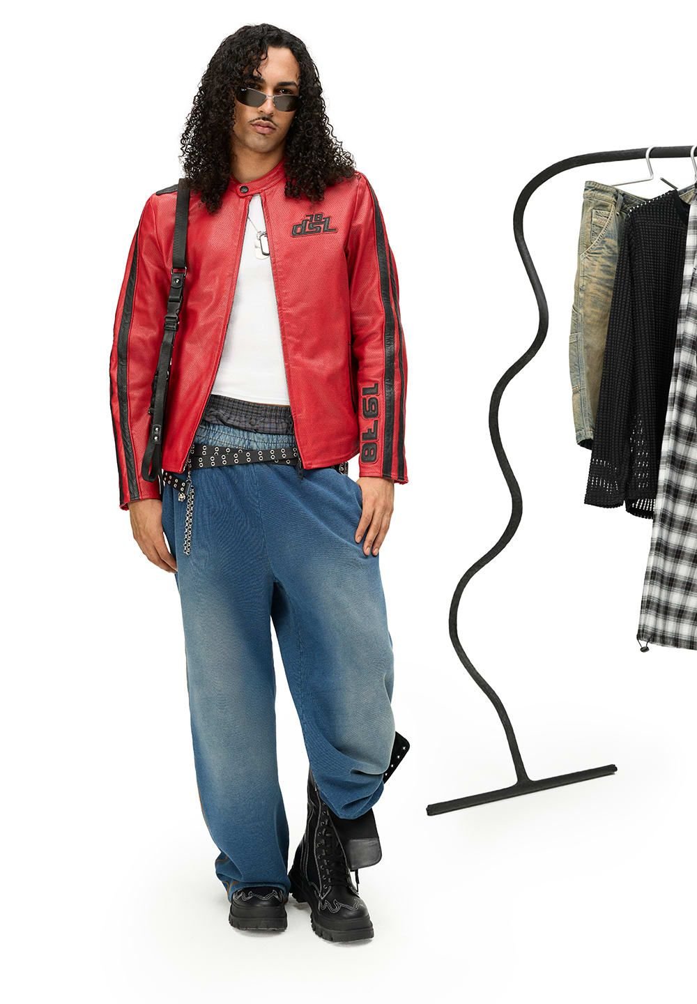 Rode leren jack met zwarte accenten en logo, witte tanktop, blauwe versleten oversized broek, en zwarte lace-up laarzen.