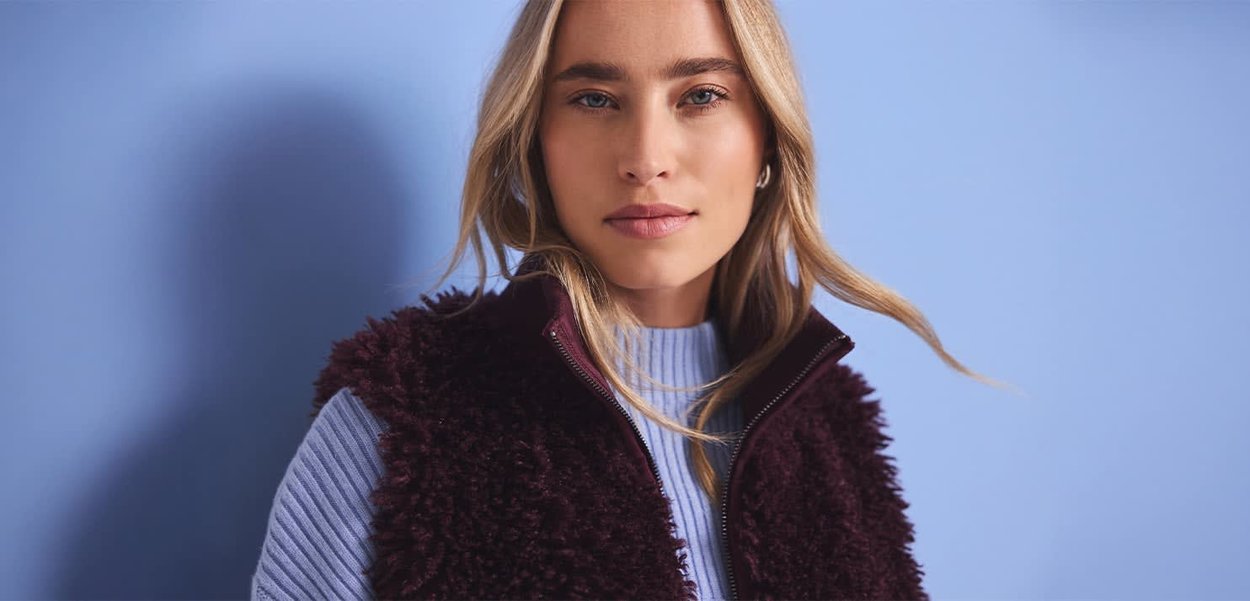 Veste sans manches en polaire bordeaux à col montant, avec fermeture éclair et tissu texturé, portée sur un pull côtelé bleu clair.