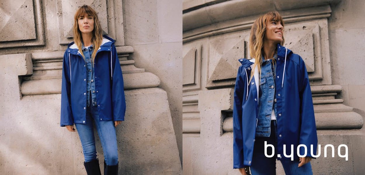 Blaue wasserdichte Jacke mit Kapuze, weißen Kordeln, Druckknöpfen und lockerer Passform, getragen über einer Jeansjacke.