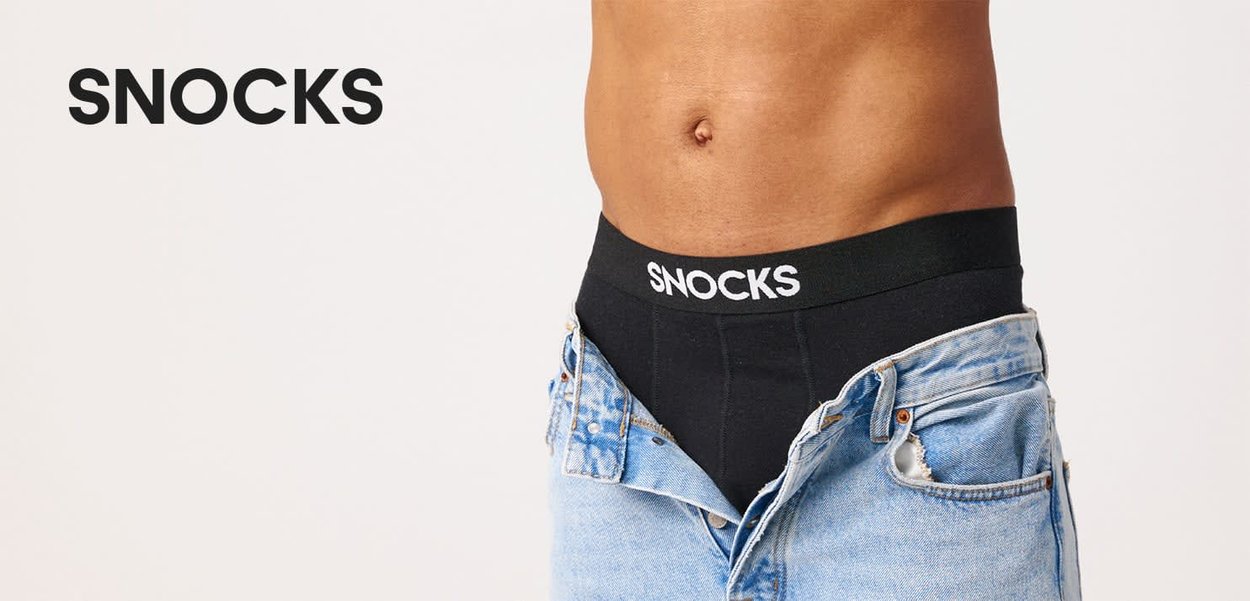 Mandligt overkrop iført sort Snocks undertøj med delvist opkneppede blå jeans mod en ensfarvet hvid baggrund.