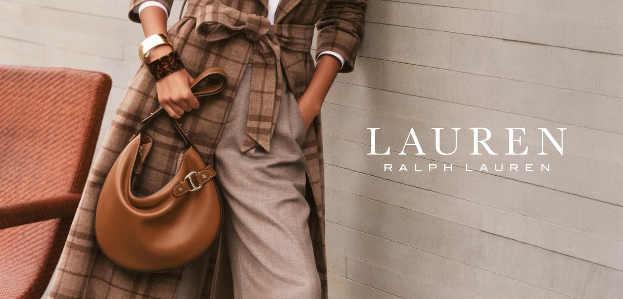 Bruine geruite jas met een strik taille, beige broek en een ronde bruine handtas met zilveren hardware tegen een minimalistische textuur achtergrond.