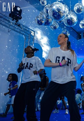 Deux personnes portant des t-shirts blancs de GAP dansent sous des boules disco suspendues avec un éclairage bleu et des reflets de lumière dispersés.