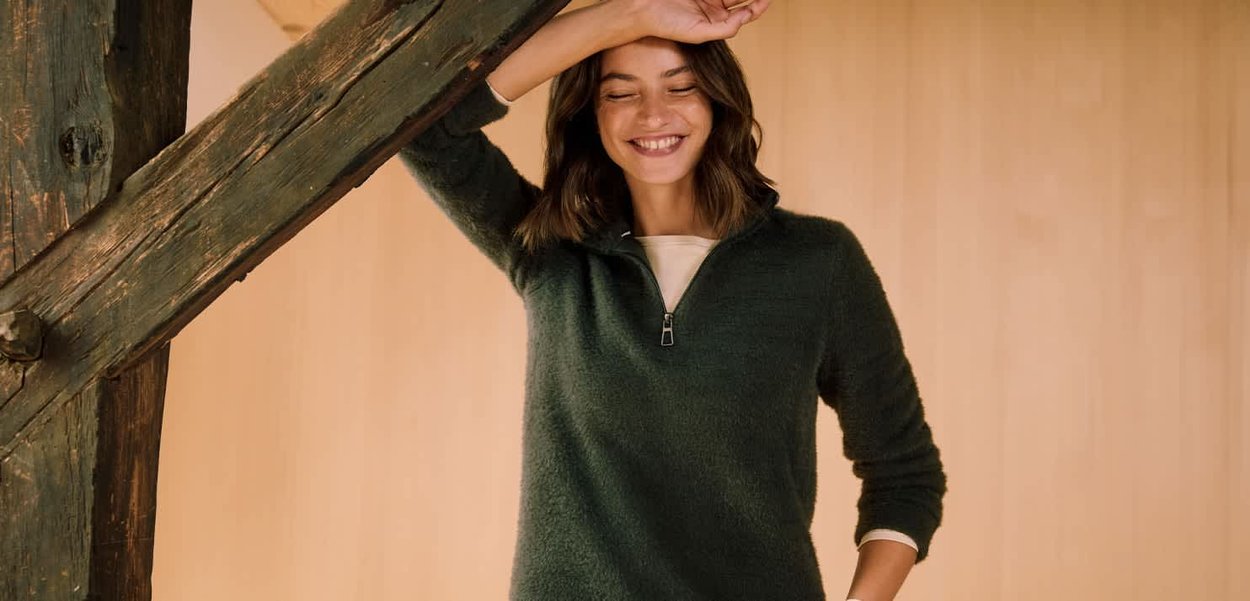 Zielony sweter na zamek wykonany z miękkiego, teksturowanego materiału. Posiada stojący kołnierz i długie rękawy, noszony na jaśniejszej koszuli.