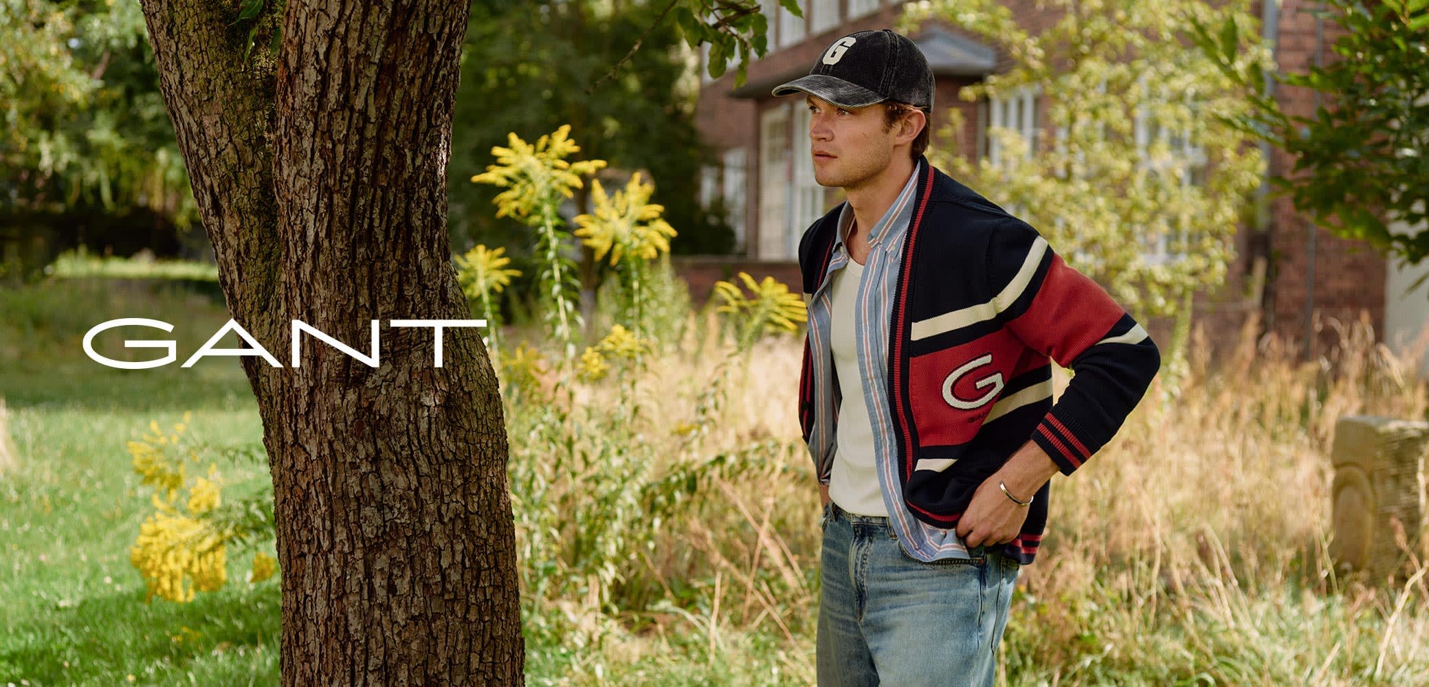 Navy and red striped cardigan over a light blue shirt, paired with light wash jeans. Casual look against a natural outdoor backdrop.