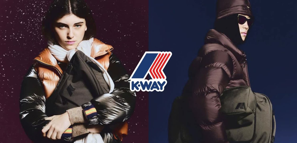 Due persone indossano giacche imbottite; una ha un cappotto arancione e nero, l'altra una giacca marrone scuro. Entrambe tengono una borsa nera con un logo.