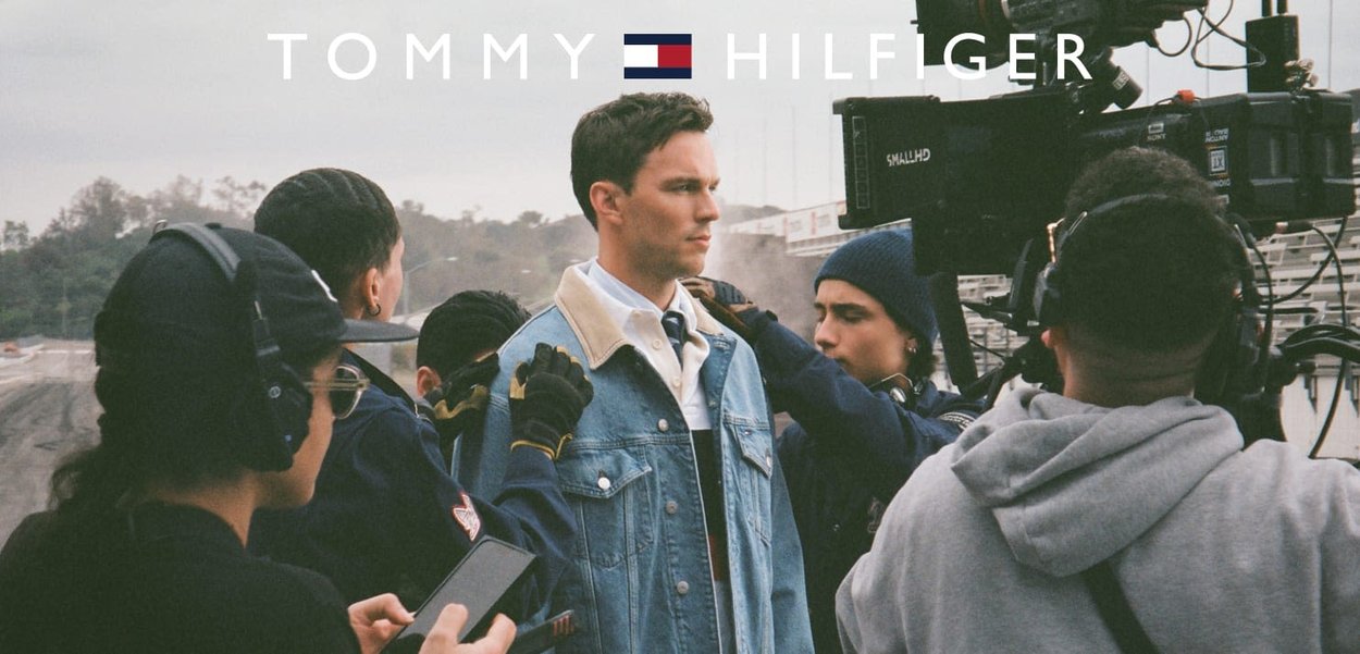 Veste en denim avec un délavage bleu clair et un col contrastant, portée sur une chemise blanche. Groupe de personnes se préparant pour une séance photo ou un tournage.