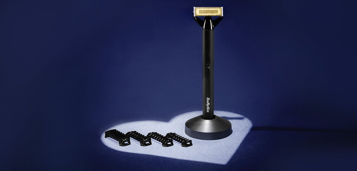 Svart Babyliss-barberhøvel med stativ ved siden av fire svarte hårklemmer, spotlys kaster en hjerteformet skygge på mørk blå bakgrunn.