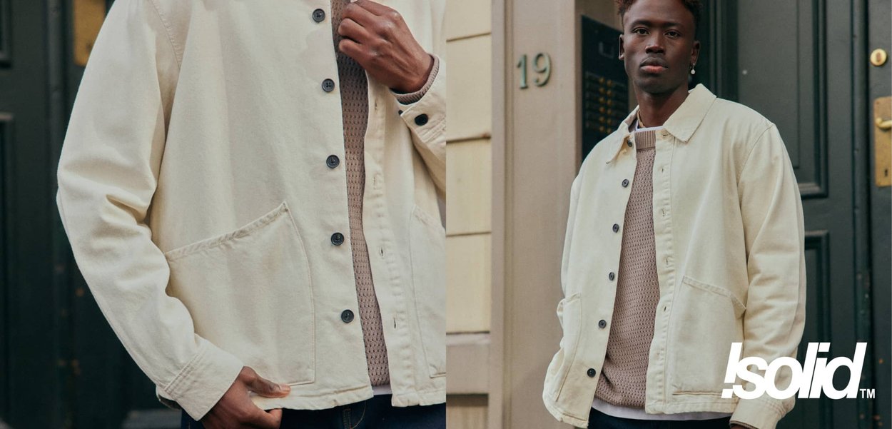 Cremefarbene Baumwolljacke mit durchgehendem Knopfverschluss, zwei Fronttaschen und lockerem Schnitt, getragen über einem strukturierten beigen Pullover.