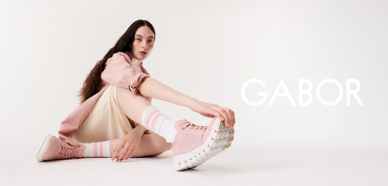 Femme étirant la jambe vers l'avant, portant des baskets roses, des chaussettes rayées et des vêtements légers sur un fond blanc avec le texte "GABOR".