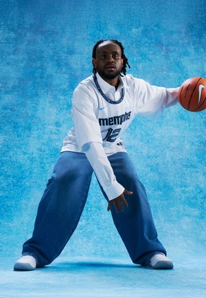 Mężczyzna w koszulce do koszykówki Memphis, kozłujący piłkę do koszykówki, ubrany w białą koszulę i szerokie niebieskie dżinsy na tle o niebieskiej teksturze.