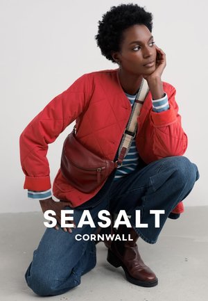 Rote gesteppte Jacke mit einem gestreiften blau-weißen Hemd, blauen Denim-Jeans und braunen Leder-Stiefeletten; lässig getragene braune Umhängetasche.