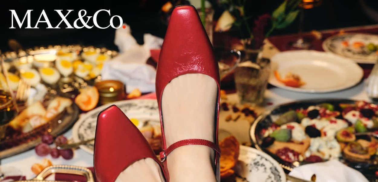 Rote Mary Jane Schuhe aus Leder, getragen an einem Fuß, der über einem Tisch mit verschiedenen Tellern mit Essen und Getränken positioniert ist.