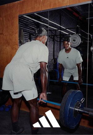 A person performing a deadlift in a gym, wearing a light gray short-sleeve shirt and white shorts, using a blue weight bar. Mirror in background.