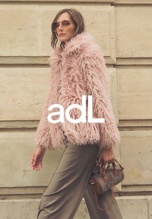 Rosa, flauschige Kunstfelljacke mit weiten Ärmeln, kombiniert mit hoch taillierten gemusterten Hosen und einer kleinen braunen Handtasche.