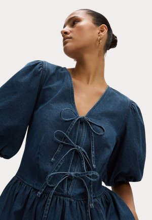Robe en denim avec un décolleté en V profond, des manches bouffantes et une jupe froncée. Présente des détails à nouer à l'avant et une couleur bleu riche.