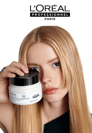 La maschera per capelli Metal DX di L’Oréal Professionnel in un contenitore rotondo bianco con un coperchio nero, posato contro i lunghi capelli biondi lisci di un modello.