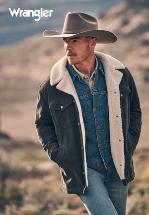 Wrangler-jakke med mørkegrønt stoff, hvit kunstpelskrage og denimoverlegg, kombinert med lyseblå jeans og bredbremmet hatt.