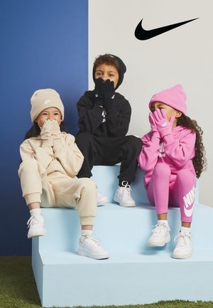 Trois enfants sont assis sur une marche bleu clair. Ils portent des sweats à capuche et des pantalons de jogging Nike en beige, noir et rose, avec des bonnets assortis et des baskets blanches.