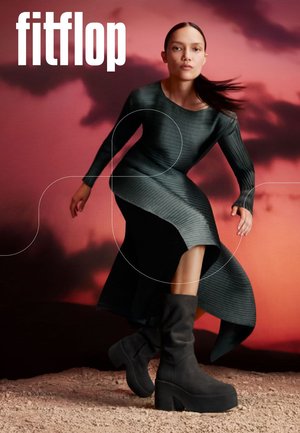 Schwarze Plateau-Stiefel mit weicher Stoffstruktur und weitem Umschlag ergänzen ein geripptes, dunkelgrünes Kleid mit fließendem Saum.