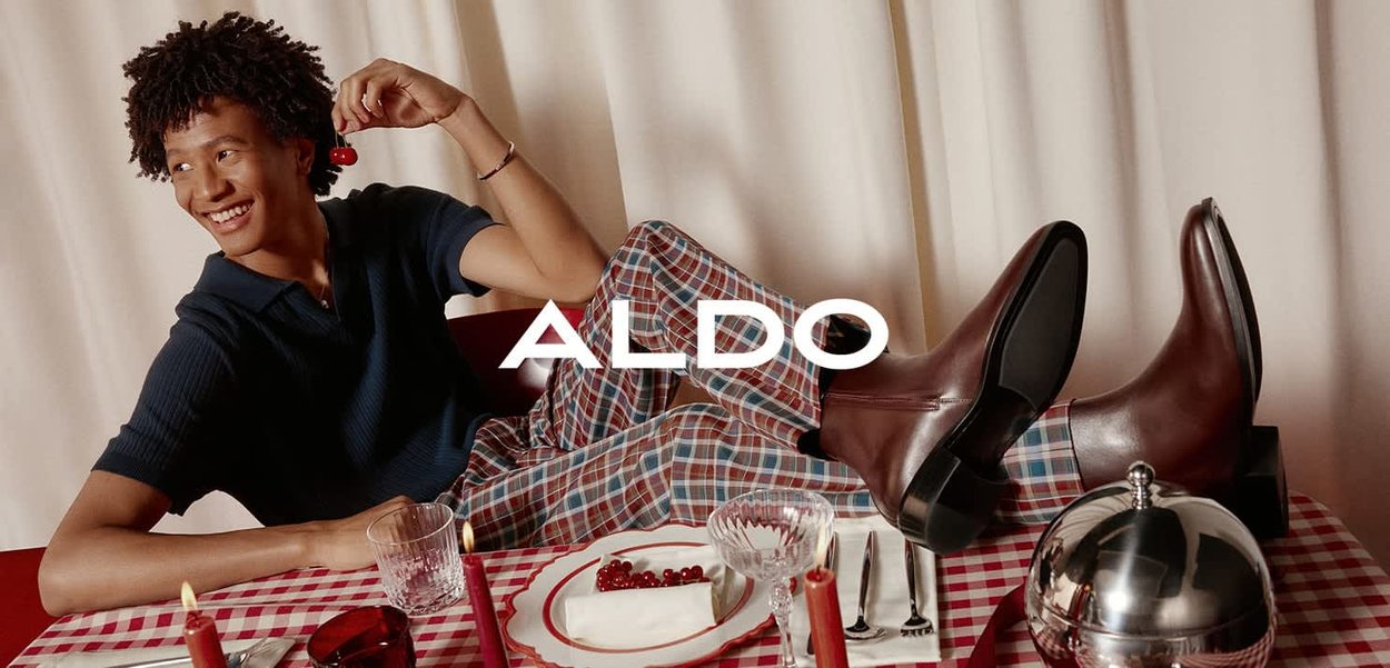 Braune Leder-Stiefel bis zur Knöchel mit glatter Oberfläche, auf einem karierten Tischdecken platziert. Das Modell trägt ein dunkles Polohemd und gemusterte Hose.