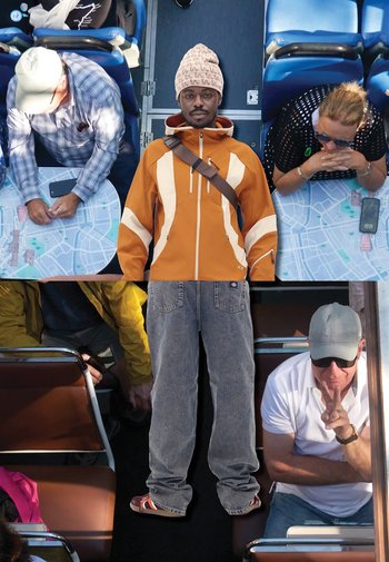 Oranje jack met witte accenten, grijze spijkerbroek en een gebreide muts. Op de achtergrond staan mensen aan een tafel met kaarten en telefoons.