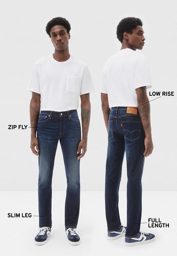 Jeans de pierna estrecha en azul oscuro con cremallera y cintura baja, con costuras en contraste y un parche de cuero en la parte trasera. Largo completo.