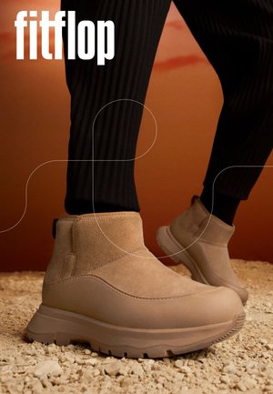 Beige Wildleder-Stiefeletten mit dicker Gummisohle. Sie zeichnen sich durch eine glatte Textur, ein minimalistisches Design und einen Schlupf-Stil aus. Stehen auf Kieselboden.