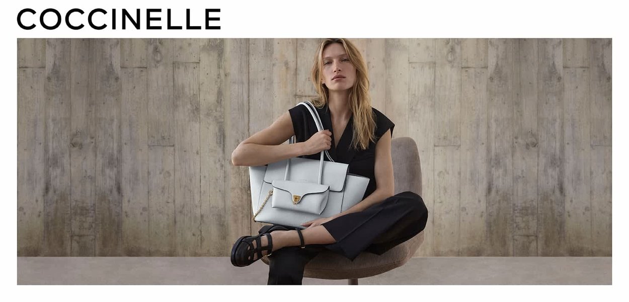 Bolso de mano de cuero gris claro con un diseño estructurado, que cuenta con una solapa frontal, herrajes dorados, doble asa y una correa de cadena desmontable.