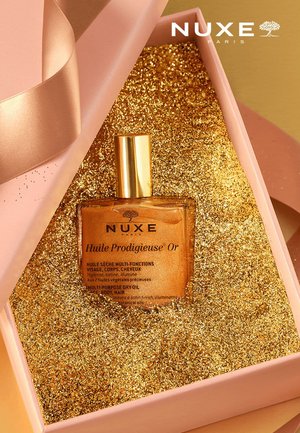 Bouteille en verre de NUXE Huile Prodigieuse Or avec des reflets dorés, présentée dans une boîte rose doublée de paillettes dorées. Bouchon doré, liquide transparent.