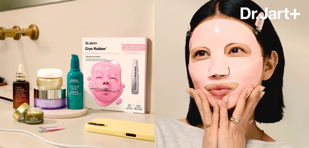 Kobieta z krótkimi czarnymi włosami, nosząca różową maseczkę do pielęgnacji skóry przymocowaną klipsami do włosów, delikatnie dotykająca twarzy dłońmi z pierścionkami.