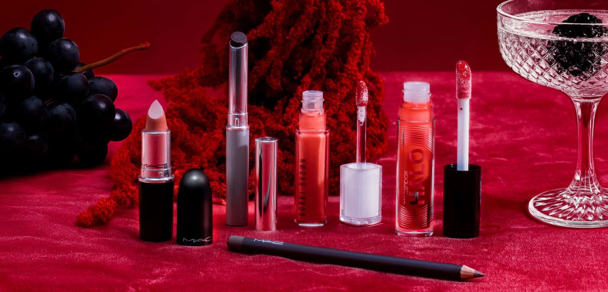 Diverse lipproducten uitgestald, met een mix van matte en glanzende texturen, in tinten variërend van nude tot levendig rood, op een rode achtergrond.