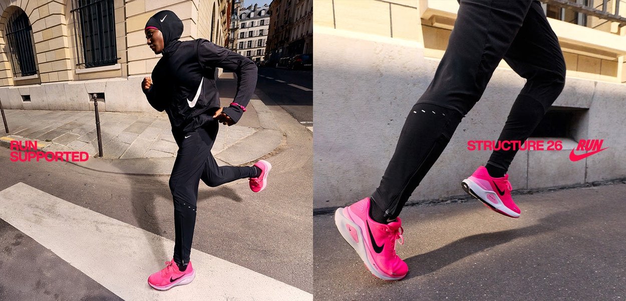 Completo sportivo nero con accenti rosa, scarpe da corsa di un brillante colore rosa, caratterizzato da un grande logo, su una strada cittadina con dettagli architettonici.