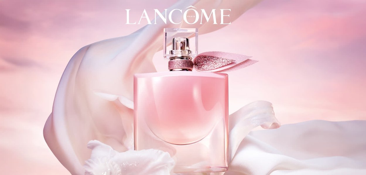 Rosa Glasparfümflasche mit einer runden Form, glitzerndem rosa Bandakzent und einem klaren Deckel. Weicher Stoffhintergrund in sanften Farbtönen.