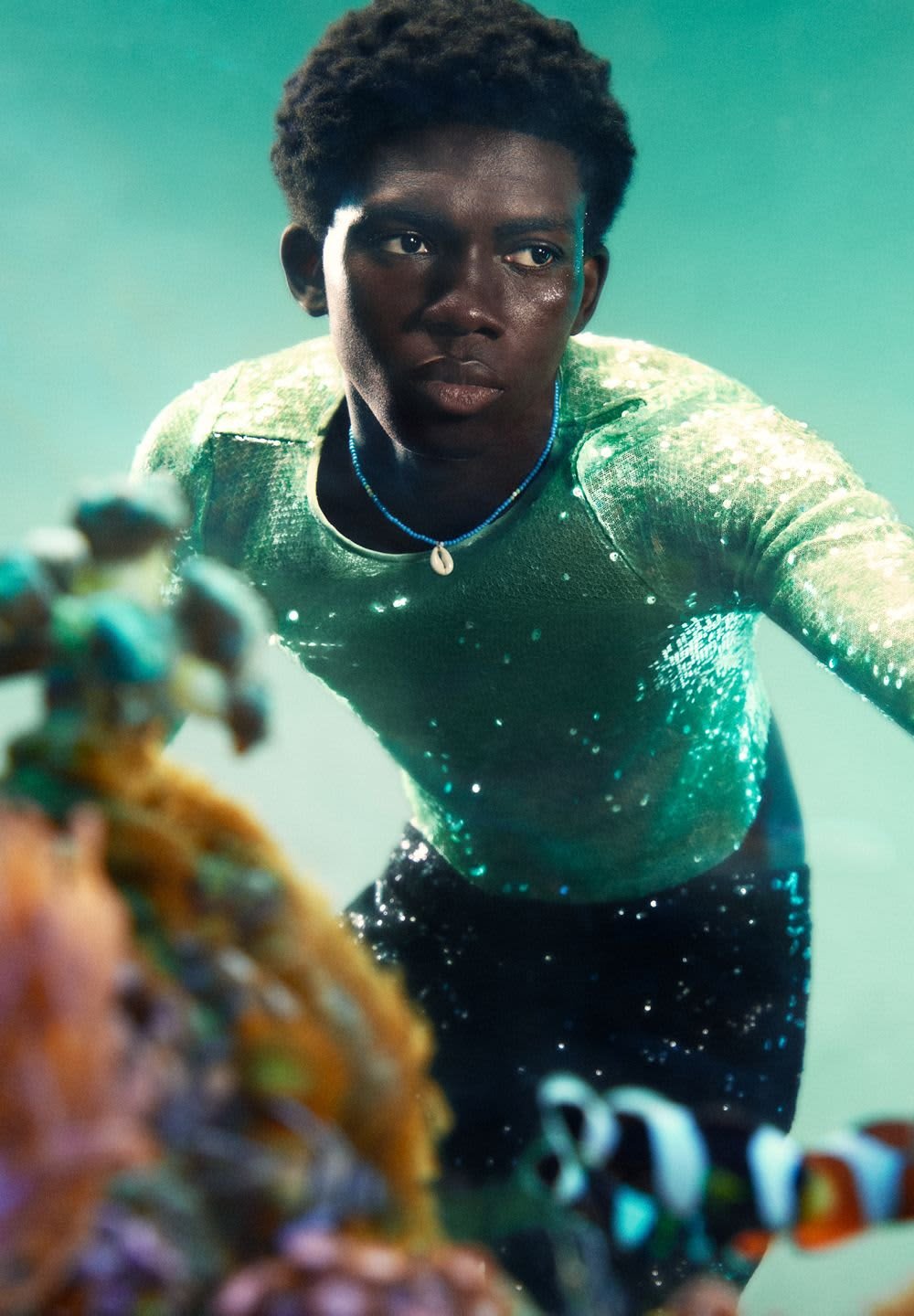 Shimmery green sequined shirt with long sleeves, black trousers, and a shell necklace, set against an underwater backdrop.