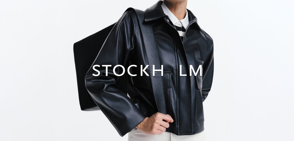 Persoon die een zwart leren jas draagt en een grote zwarte rugzak over één schouder draagt tegen een witte achtergrond.