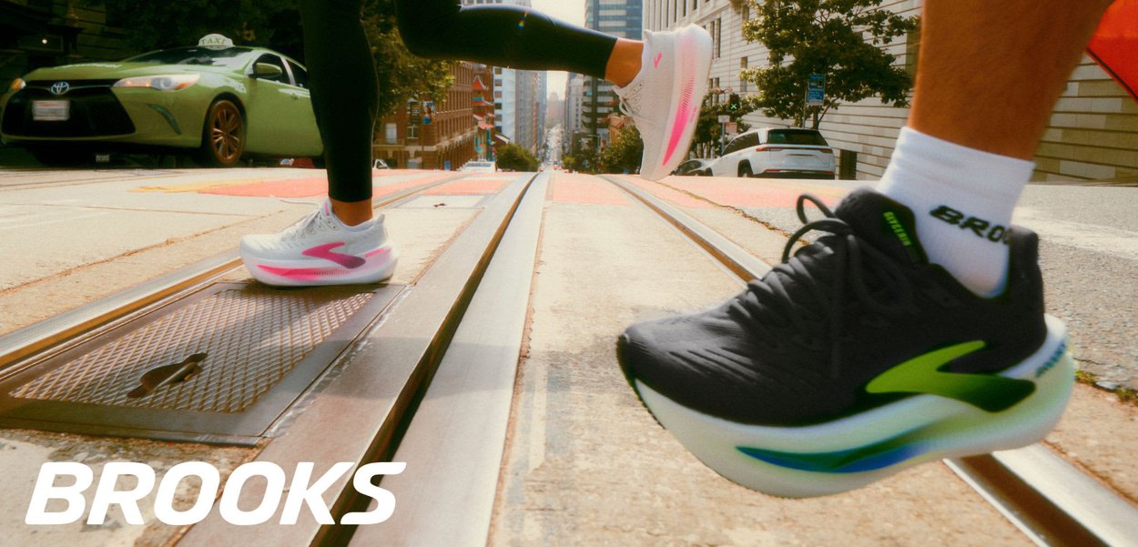 Running shoes by Brooks: light grey upper, pink and white sole, textured mesh, with reflective accents; black shoe with green details also visible.