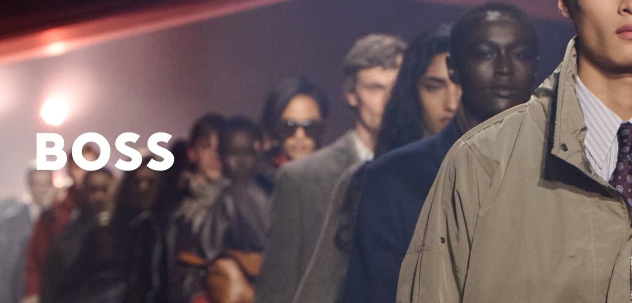 Diverse modellen lopen op de catwalk van een modeshow, gekleed in stijlvolle kleding, met het BOSS-logo zichtbaar aan de linkerkant.