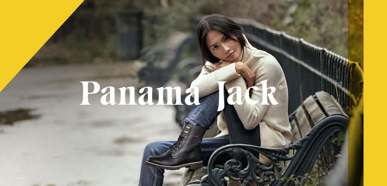 Zwarte leren enkellaarzen met vetersluiting aan de voorkant, gouden accenten en een robuuste zool. Model draagt een beige sweater en jeans, zittend op een bank.